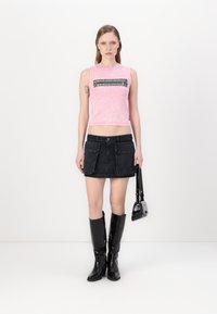 Rosa cropped tank top med svart grafisk detalj, paret med en svart denimskjørt med frampokker og knelang, glanset svart støvler.