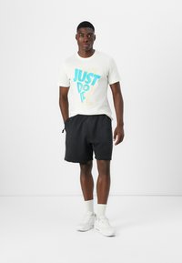 Bela majica s kratkimi rokavi in turkiznim napisom "SAMO NAREDITE TO"; v kombinaciji z črnimi kratkimi hlačami, belimi supergami in belimi nogavicami do gležnjev.