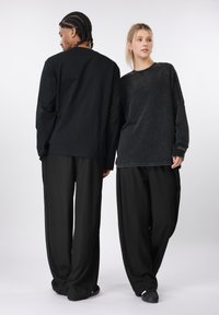 Μαύρα μακρυμάνικα τοπ, το ένα με λεία υφή, το άλλο με ξεθωριασμένο φινίρισμα· και τα δύο σε συνδυασμό με φαρδιά μαύρη παντελόνια.