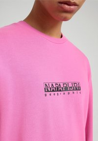 Felpa a maniche lunghe rosa realizzata in tessuto morbido, con un logo stampato nero nella zona del petto e un collo rotondo.