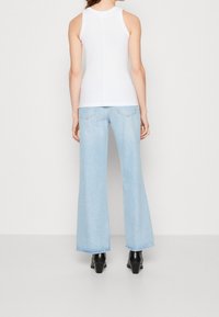 Bílý top bez rukávů zkombinovaný se světle modrými zvonovými džíny. Džíny mají design s pěti kapsami a jemně roztrhaný lem. Černé boty na podpatku.