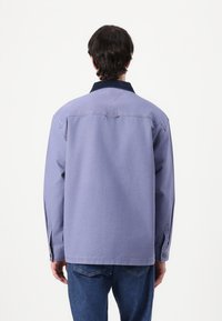 Purple shirt with a dark collar, long sleeves, and button cuffs. The back features a simple design and loose fit, paired with blue jeans.