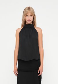 Top preto de halter feito de tecido leve, com decote franzido e ajuste fluido, combinado com uma saia preta justa.
