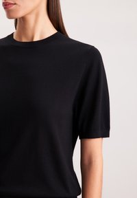 Czarny, dziany sweter z krótkim rękawem, o okrągłym dekolcie, z gładką teksturą i dopasowanym krojem. Prosty, minimalistyczny design.