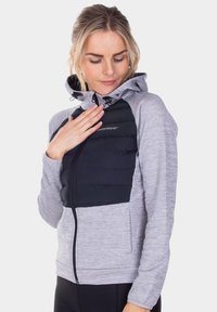Dames zip-up jack met een grijze binnenkant, zwart gewatteerd voorpaneel, capuchon met trekkoorden en elastische manchetten. Voorzien van zijzakken.