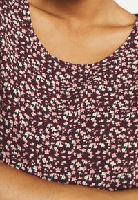 Top burdeos con flores que presenta un escote redondeado, pequeños patrones florales en rosa y verde, y una tela suave y texturizada.