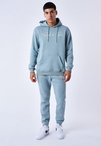 Ensemble de sweat à capuche bleu clair et de pantalons de jogging, comprenant une poche avant et un logo blanc. Confectionné en tissu doux avec une texture lisse.