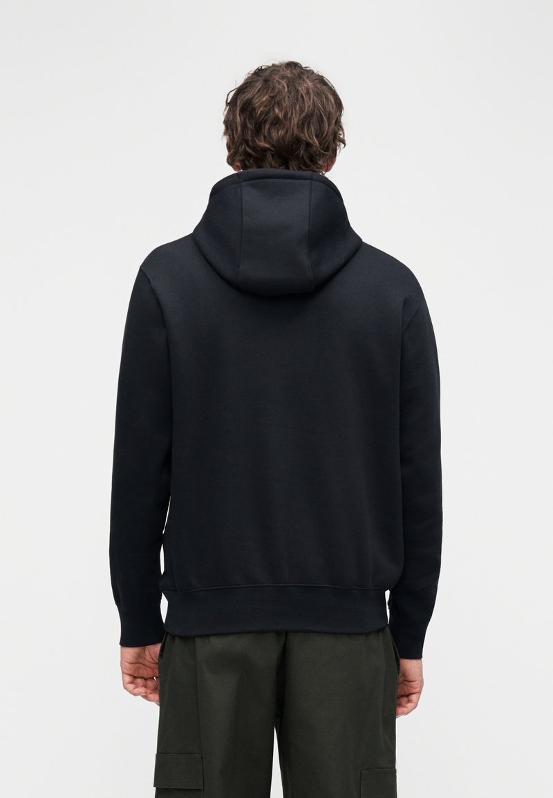 Black hooded sweatshirt made of cotton blend, featuring a simple design, ribbed cuffs, and a relaxed fit, paired with olive green cargo pants.