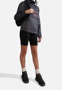 Grå letvægtsjakke med logo, sorte cykelshorts og sorte vandresko. Sokkerne er i kremfarve og ribbede.