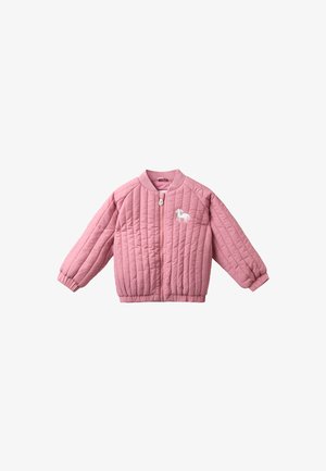Lachend jong meisje zit op een oranje vloer, draagt een roze winterjas, bloemenlegging, gebreide muts met pompon, wanten en donkerroze laarzen.