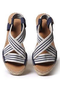 Une paire de sandales beiges avec des sangles entrecroisées bleu marine et blanches et des semelles en jute cousues, présentée sur un fond blanc.