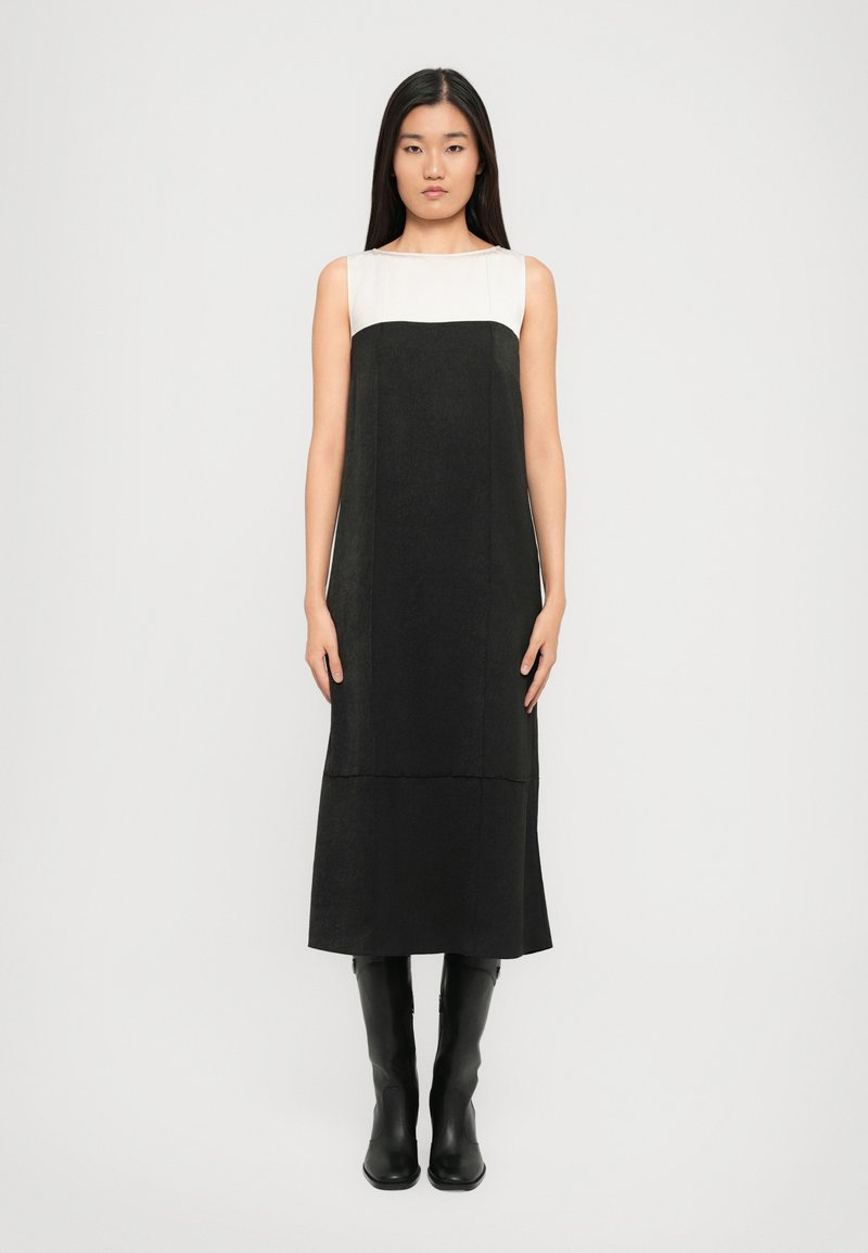 Mustmust värvi, ilma varrukateta kleit koos valge ülemise osaga. Valmistatud tekstureeritud kangast, millel on minimalistlik disain ja keskmise pikkusega äär.