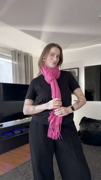 Rozā bārkstainais šalle ap kaklu, valkāts kopā ar melnu T-kreklu un melnām biksēm. Gluda auduma tekstūra pret neitrālu fonu.