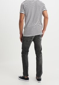 Jeans grises de corte slim y cinco bolsillos, combinados con una camisa de manga corta a rayas en blanco y negro, y zapatillas de lona negras.
