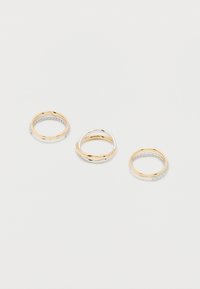 Τρία χρυσά και ασημένια δαχτυλίδια σε λευκό φόντο, δύο με μικρά διαμάντια και ένα με αλληλοσυνδεδεμένες απλές μπάντες.