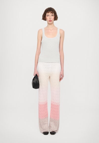 Top sin mangas gris con textura en relieve combinado con pantalones de patrón en chevron en tonos degradados que van del crema al rosa, completado con un bolso de mano negro.