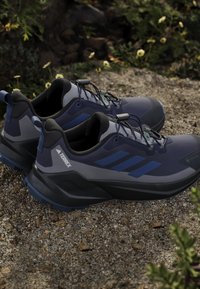 Scarpe da ginnastica navy e grigie con una tomaia testurizzata, caratterizzate da dettagli neri, suola in gomma e lacci fissati da toggle.