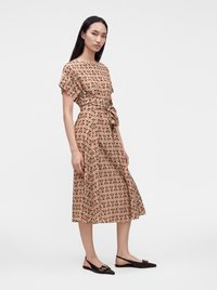 Femme portant une robe à motifs, courte aux genoux, à manches courtes, avec une ceinture nouée à la taille et des chaussures plates slingback noires.