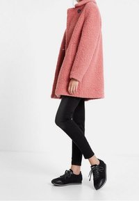 Roze getextureerde wollen jas met een hoge kraag, knoopdetails, gecombineerd met zwarte skinny jeans en zwarte veterschoenen.