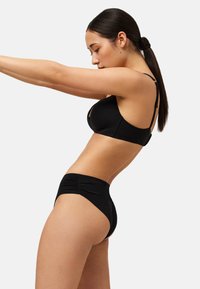 Sostén negro y braguitas de talle alto hechas de tela lisa, con un sutil detalle fruncido en la cinturilla y tirantes ajustables.