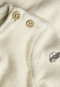 Strikket sweater i cremet farve med struktureret stof, med to træknapper på skulderen og en broderet bil-detalje.