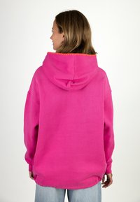 Oversized pink hoodie with a drawstring hood, featuring orange stitching along the edge. The fabric appears soft with a smooth texture.