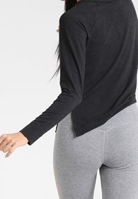 Maglietta nera a maniche lunghe con scollo rotondo, abbinata a leggins grigi. La maglietta presenta una vestibilità comoda e un leggero orlo posteriore.