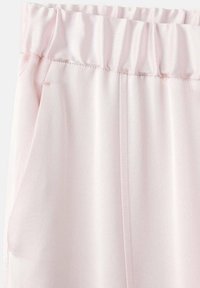 Pantalons en tissu rose clair doux, léger, dotés d'une taille élastique et de poches latérales, avec une texture lisse et un design minimaliste.