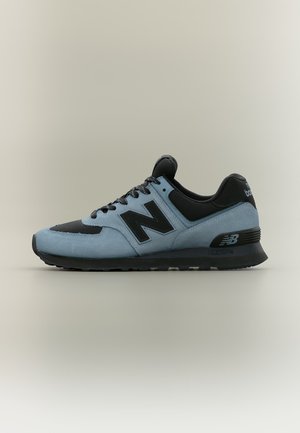 Светлосиньо и черно спортно обувки New Balance с черни връзки и лого отстрани, изложени на неутрален фон.