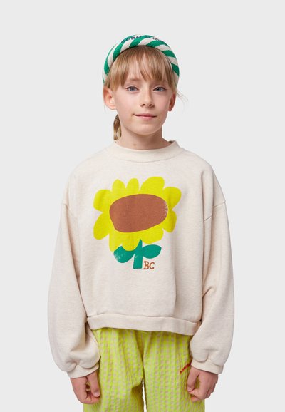 Cream-colored oversized sweatshirt with a large sunflower graphic in yellow, brown, and green, paired with textured green pants.