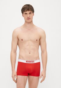 Sarkanas bokseršorti ar ciešu pieguļamību, baltu jostas vietu ar uzrakstu "DIESEL." Gluda auduma tekstūra un vienkāršs dizains bez rakstiem.