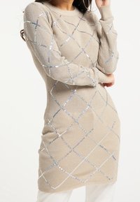 Stickad klänning i beige med en figursydd design, som har ett diamantmönster av reflexiga paljetter och ribbade ärmslut.