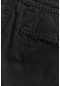 Black fabric pants featuring a back pocket, a soft texture, and a relaxed fit with an elastic waistband and neat stitching details.