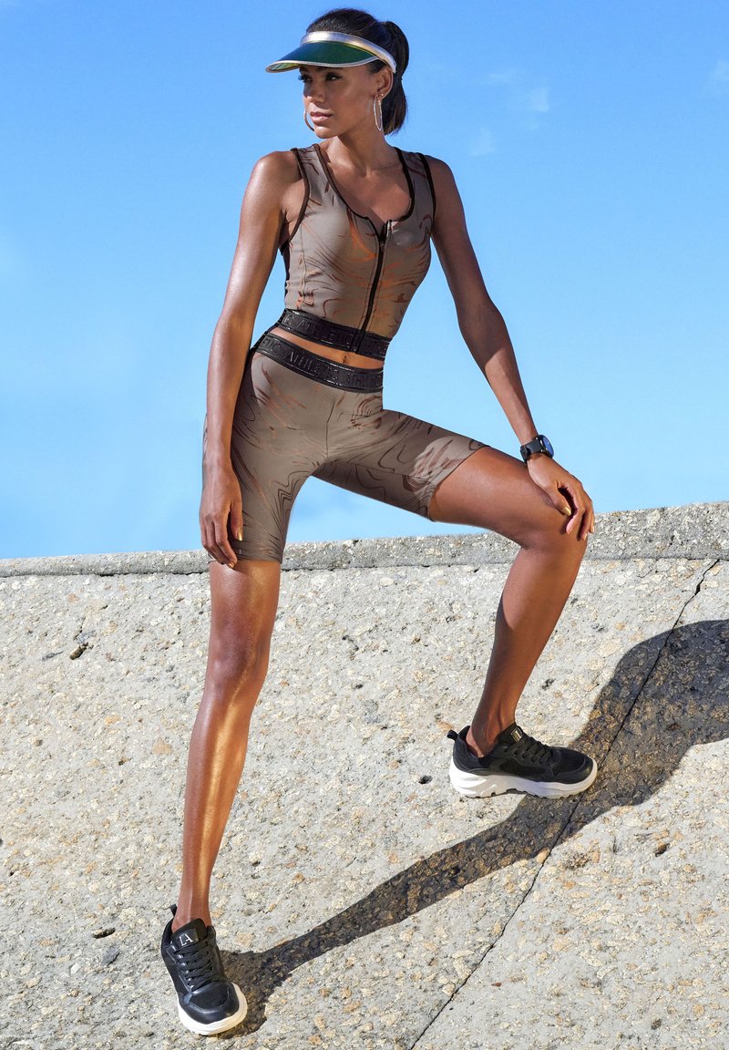 Sports outfit featuring a fitted, sleeveless top and mid-thigh shorts in tan with a subtle pattern. Black sneakers and a visor complete the look.