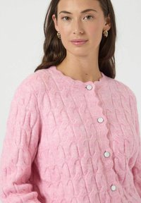 Pink strikket cardigan med et struktureret kabelmønster, rund halsudskæring og sikre lukninger med runde knapper.