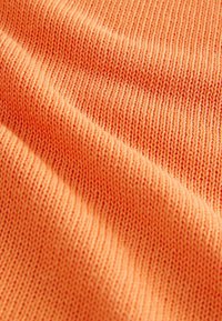 Tessuto intrecciato di un vivace arancione con una fine trama a coste. Le cuciture sono uniformi, mostrando un aspetto liscio e morbido senza pattern visibili.