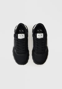 Pár čiernych tenisiek Armani Exchange s detailmi z mäsitej a kozej kože, biele logo na jazyku a vnútornej úprave, zobrazené zvrchu.