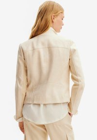 Giacca in suede beige con una vestibilità su misura, caratterizzata da un taglio dritto e dettagli di cucitura discreti, mostrata dal retro. Superficie strutturata.