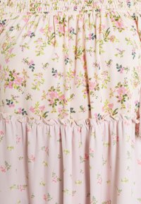 Tissu rose clair avec petites feuilles vertes et motif floral rose, avec un détail de volants froncés à la taille.