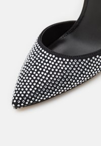 Scarpa nera con punta a punta realizzata in tessuto, impreziosita da numerosi strass argentati, con texture liscia e silhouette elegante.