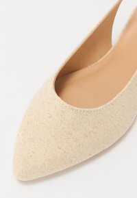 Chaussure slip-on en tissu beige avec un orteil pointu et des côtés découpés, dotée d'une doublure intérieure lisse et d'un extérieur texturé en tissé.