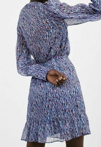 Robe à imprimé floral bleu avec des accents violets et roses, en tissu transparent, à manches longues, taille cintrée et ourlet volanté.