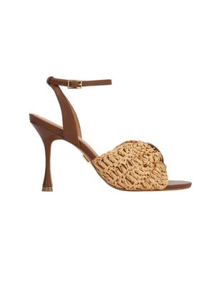 Pruun kõrge kontsaga sandaal pahkluu rihmaga ja kuldse pandlaga, millel on beežid heegeldatud esiosa rihmad ja peenike konts valgel taustal.