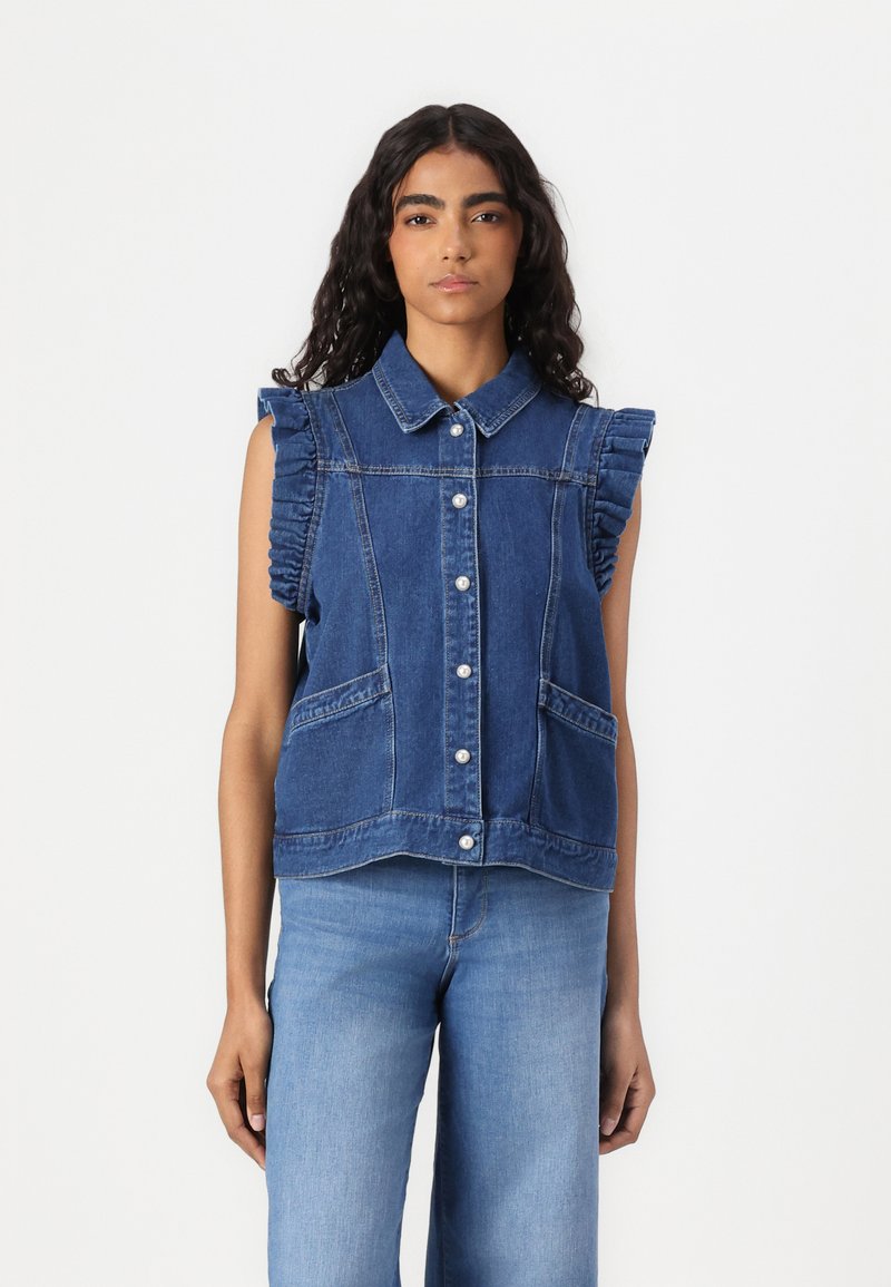 Denim vest med krage, volanger ved ermet, frontlommer og knappestengning. Tøyet er en mellomblå farge med et klassisk design.