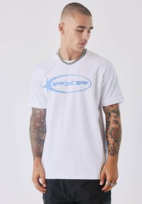 Camiseta de algodón blanca con un logo "PXP" en azul claro en el frente. Mangas cortas, cuello redondo y corte relajado con tatuajes visibles en los brazos.