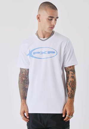 Camiseta de algodón blanca con un logo "PXP" en azul claro en el frente. Mangas cortas, cuello redondo y corte relajado con tatuajes visibles en los brazos.