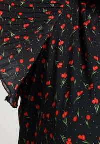 Tissu noir à motif floral de fleurs rouges et de tiges vertes, avec des détails plissés. Petits pois blancs dispersés partout.