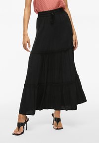 Jupe maxi noire à plusieurs niveaux avec une taille à cordon. Fabriquée en tissu léger, elle présente une finition texturée et des accents froncés à l'ourlet.