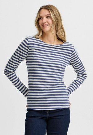 Camicia a righe a maniche lunghe in blu navy e crema, con scollatura a barca e tessuto morbido. Abbinata a jeans scuri.