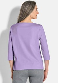 Lavendel top met driekwartmouwen gemaakt van zachte stof, met een ronde hals en een rechte snit, gecombineerd met grijze jeans.